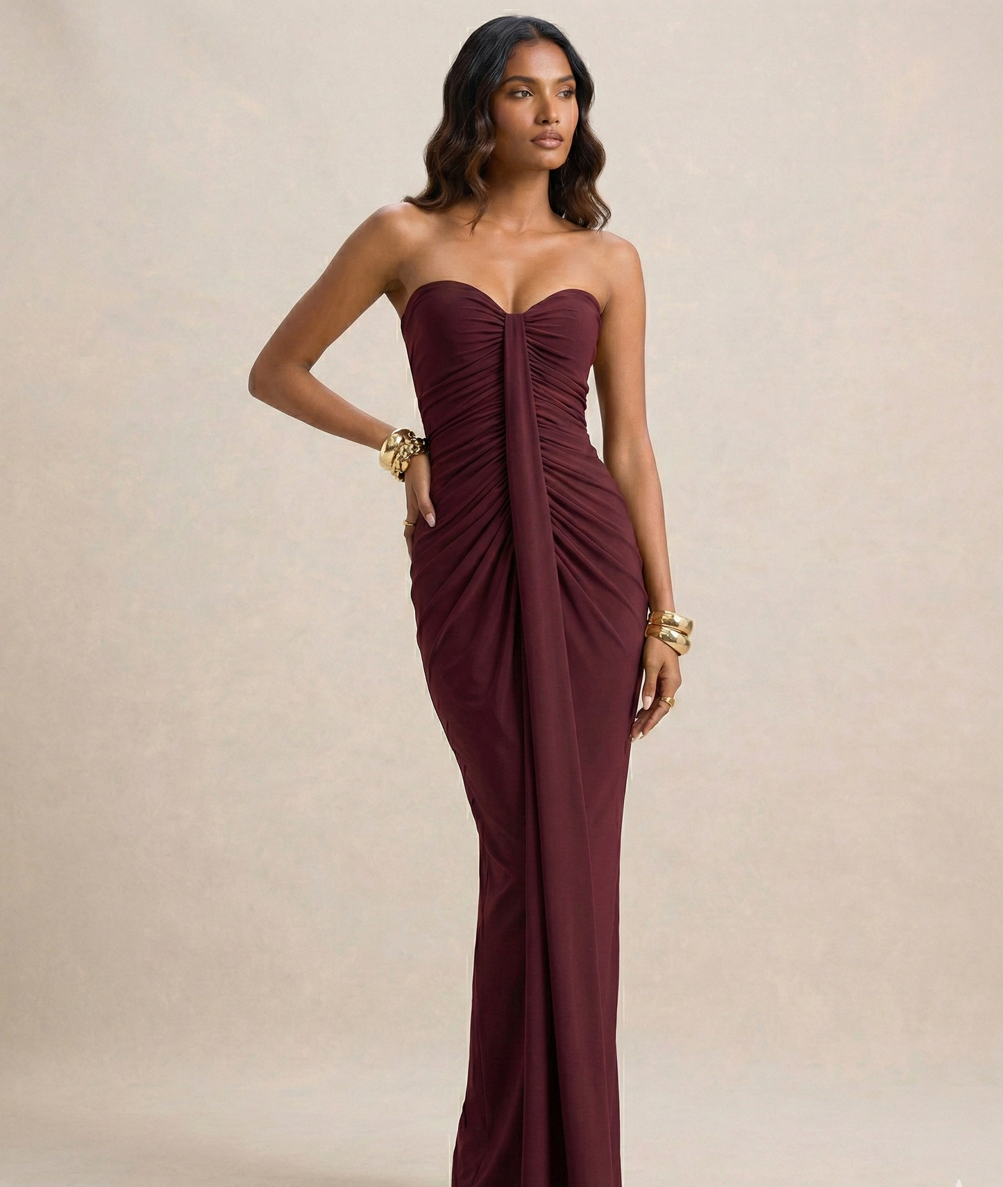 Woman wearing a strapless burgundy gown against a beige background